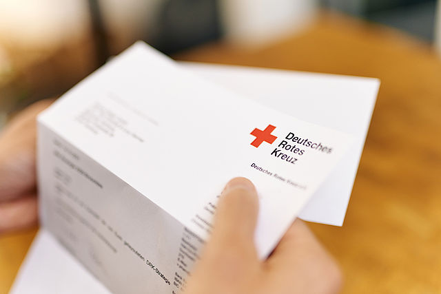 Symbolfoto Brief des DRK. Symbolfoto Brief des DRK. Hand hält Briefbogen mit dem Logo.